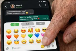 Mujer mayor feliz sonriendo sosteniendo celular con emojis y corazones en WhatsApp